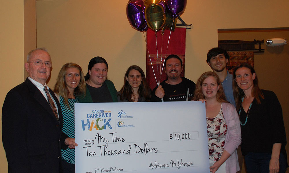 Winning team poses for the camera with several members holding a large check for $10,000.